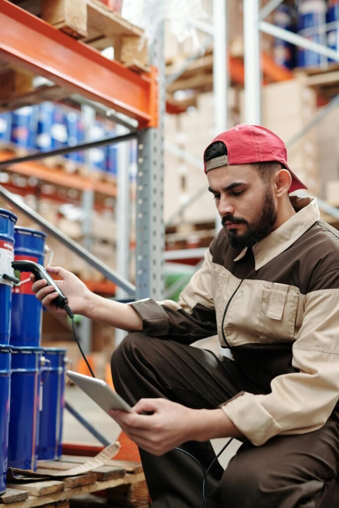 pexels-photo-4484150-4484150 Man in warehouse scanning items with digital tablet, focused on inventory management.